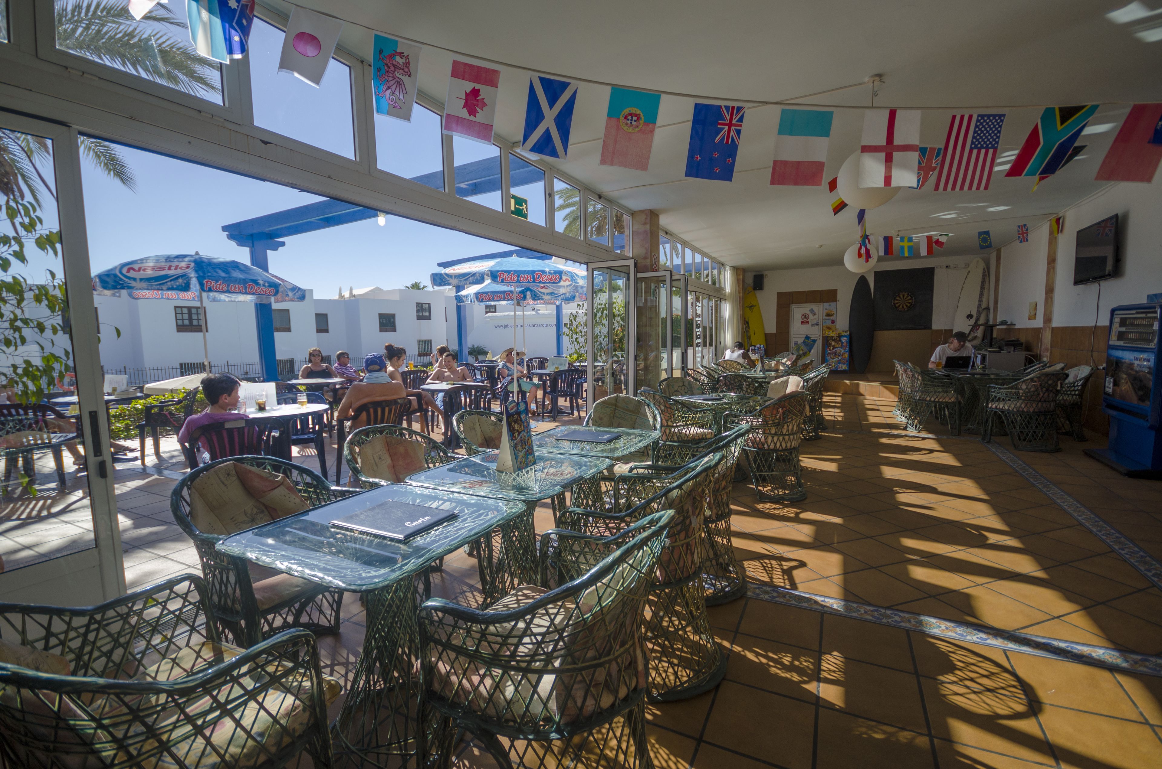 An outdoor cafe with tables and chairs, flags hanging from the ceiling, and a view of the street outside.