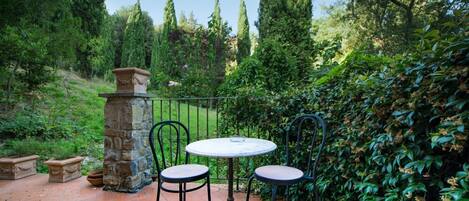 Un patio al aire libre con un pilar de piedra, dos sillas de metal y una mesa redonda.