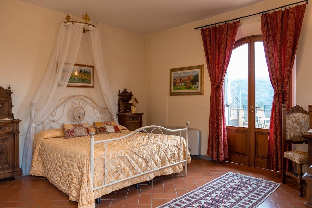 A bedroom with a bed, a nightstand, a lamp, a painting, and a view through a window.