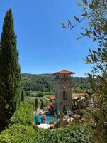 Una torre in pietra con tetto rosso che si affaccia su una piscina circondata da verde e colline.