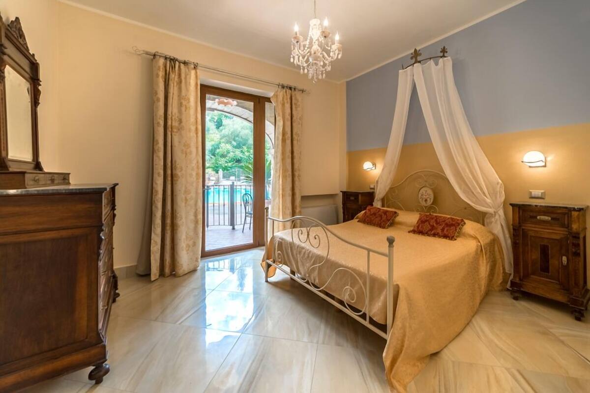 A bedroom with a bed, a chandelier, a nightstand, and a wooden dresser.