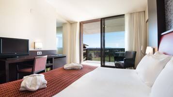 Habitación de hotel con una cama grande, un escritorio con televisor, una silla y vistas al exterior.