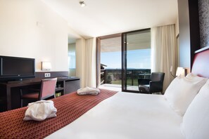 A hotel room with a large bed, a desk with a television, a chair, and a view of the outdoors. - Mas Sola (Santa Coloma de Farners)