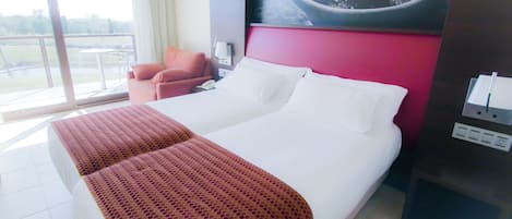 Ein Hotelzimmer mit einem großen Bett, einem Sessel, einem Schreibtisch und Blick ins Freie.