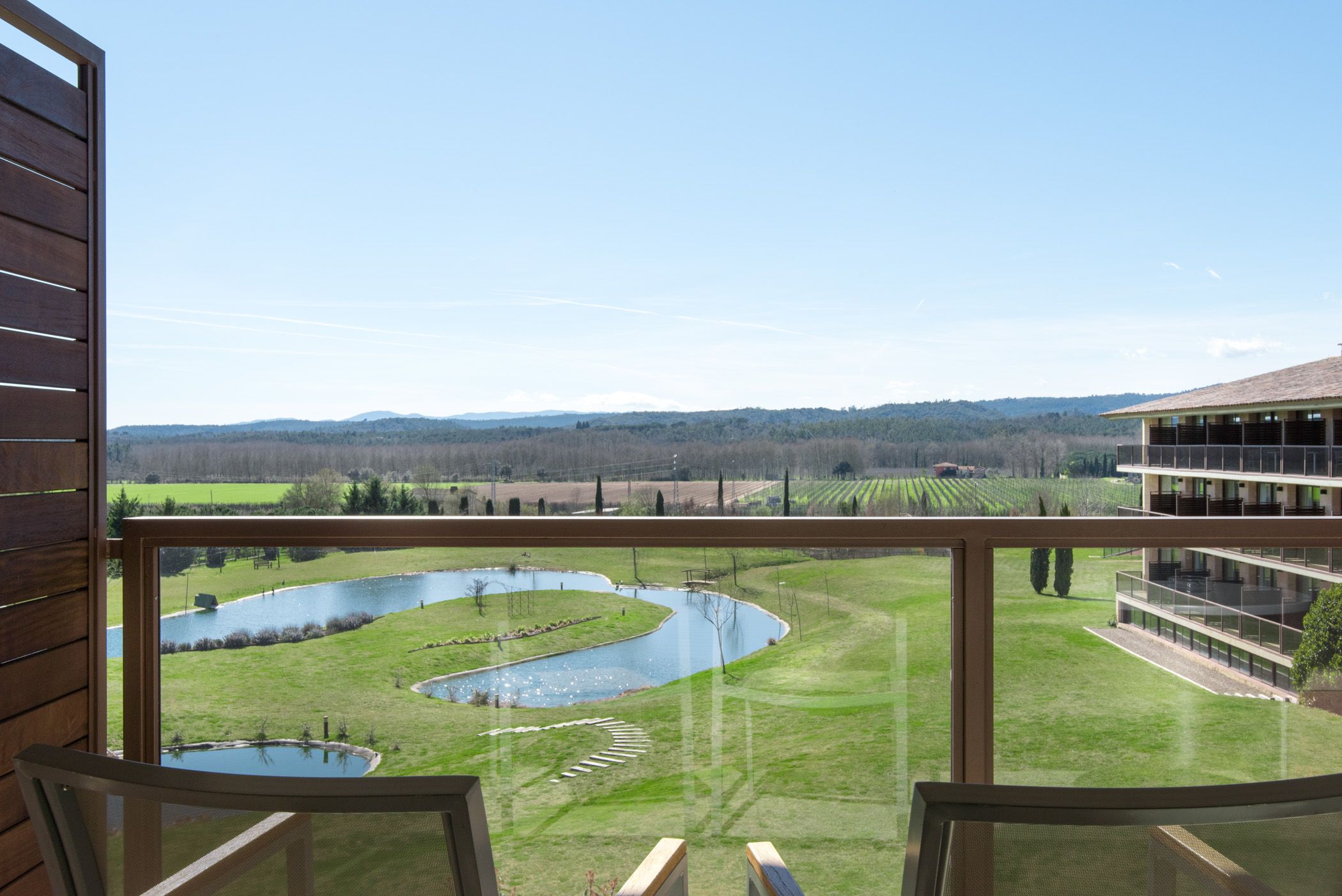 Un balcon donnant sur un espace paysager comprenant un étang et des collines lointaines.