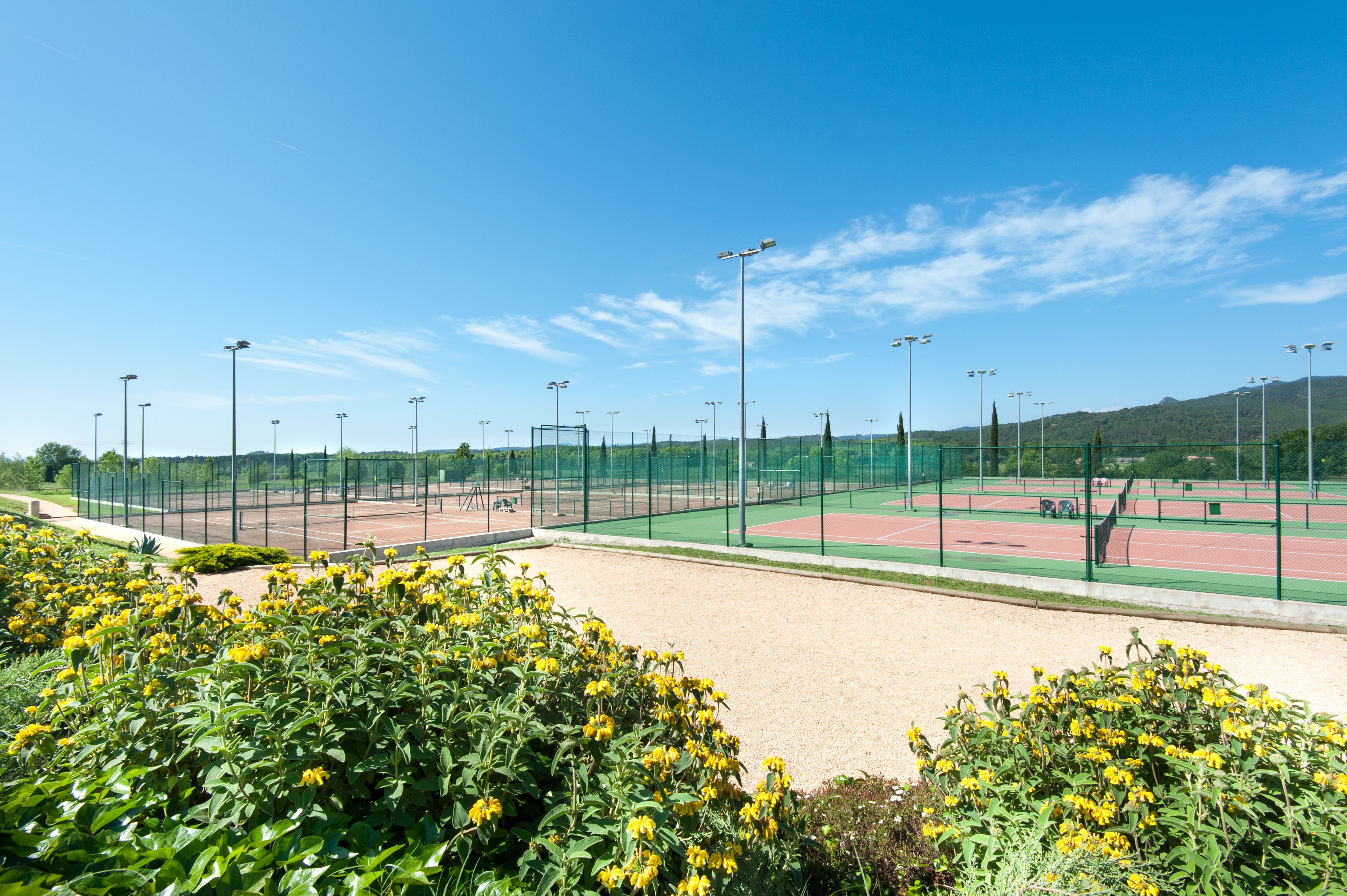 Un complexe sportif doté d’un court de tennis, entouré d’une clôture et équipé de projecteurs.