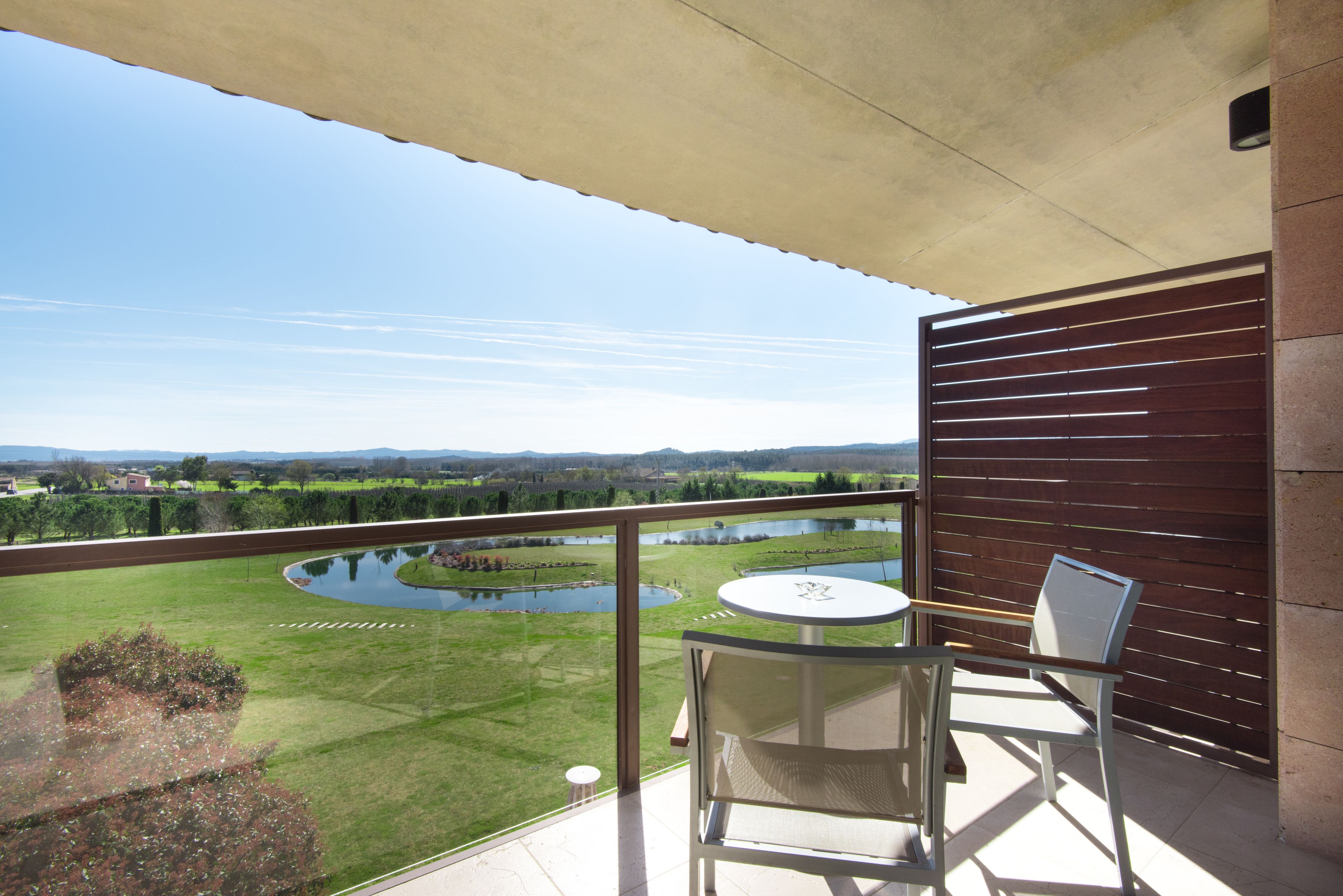 A balcony with a view of a lake, a small table, and two chairs.