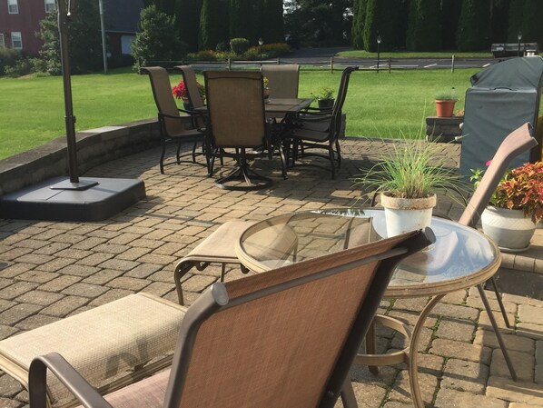 An outdoor patio with a round table and chairs, surrounded by potted plants and a grassy lawn. - Homestead Lodging (Lancaster)