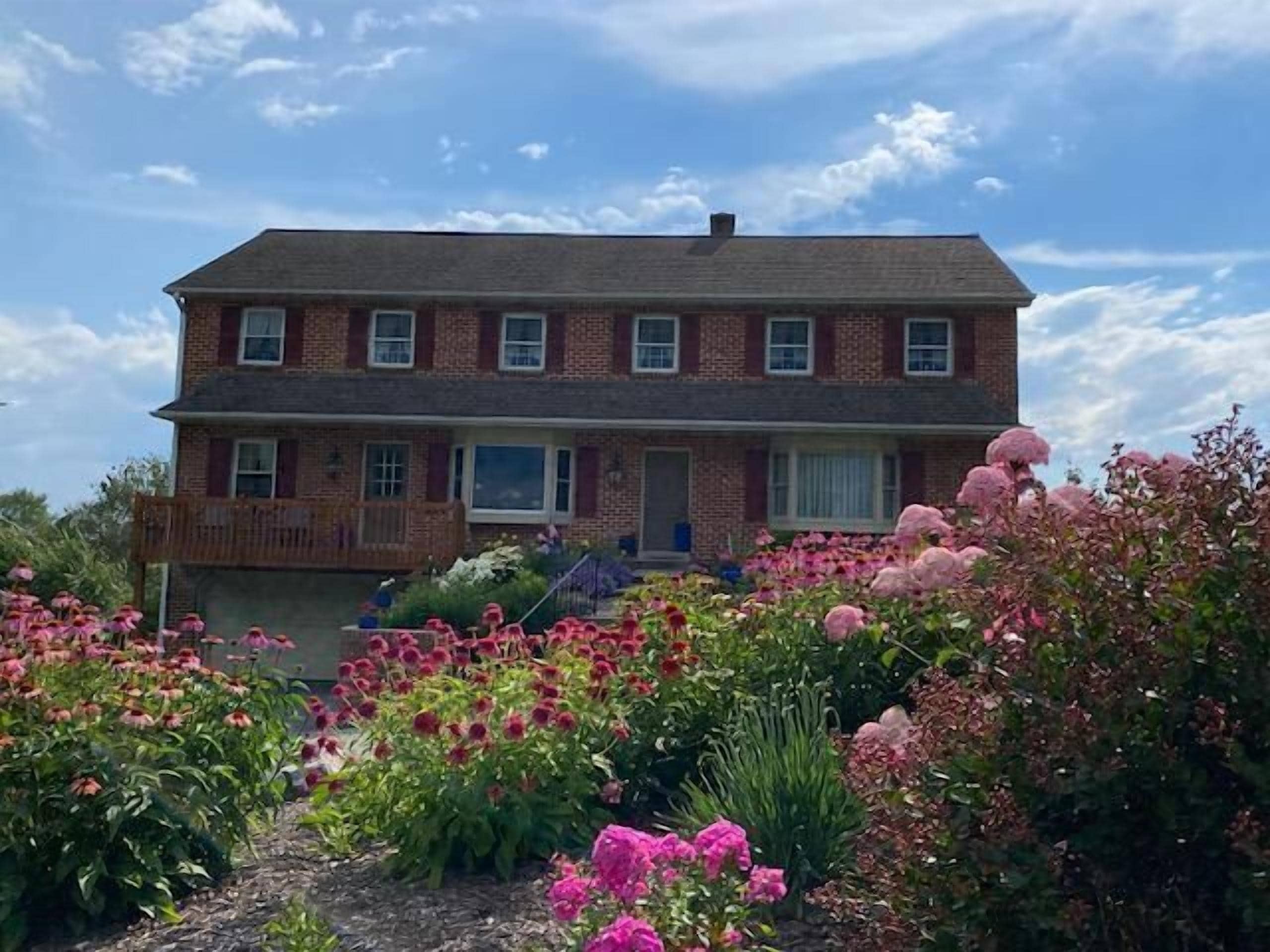 A two-story brick house with a front porch and a garden with pink flowers.