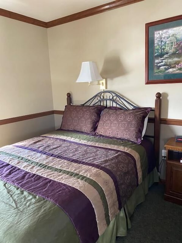 A neatly made bed with a patterned bedspread and pillows, a bedside lamp, and a framed picture on the wall. - Homestead Lodging (Lancaster)