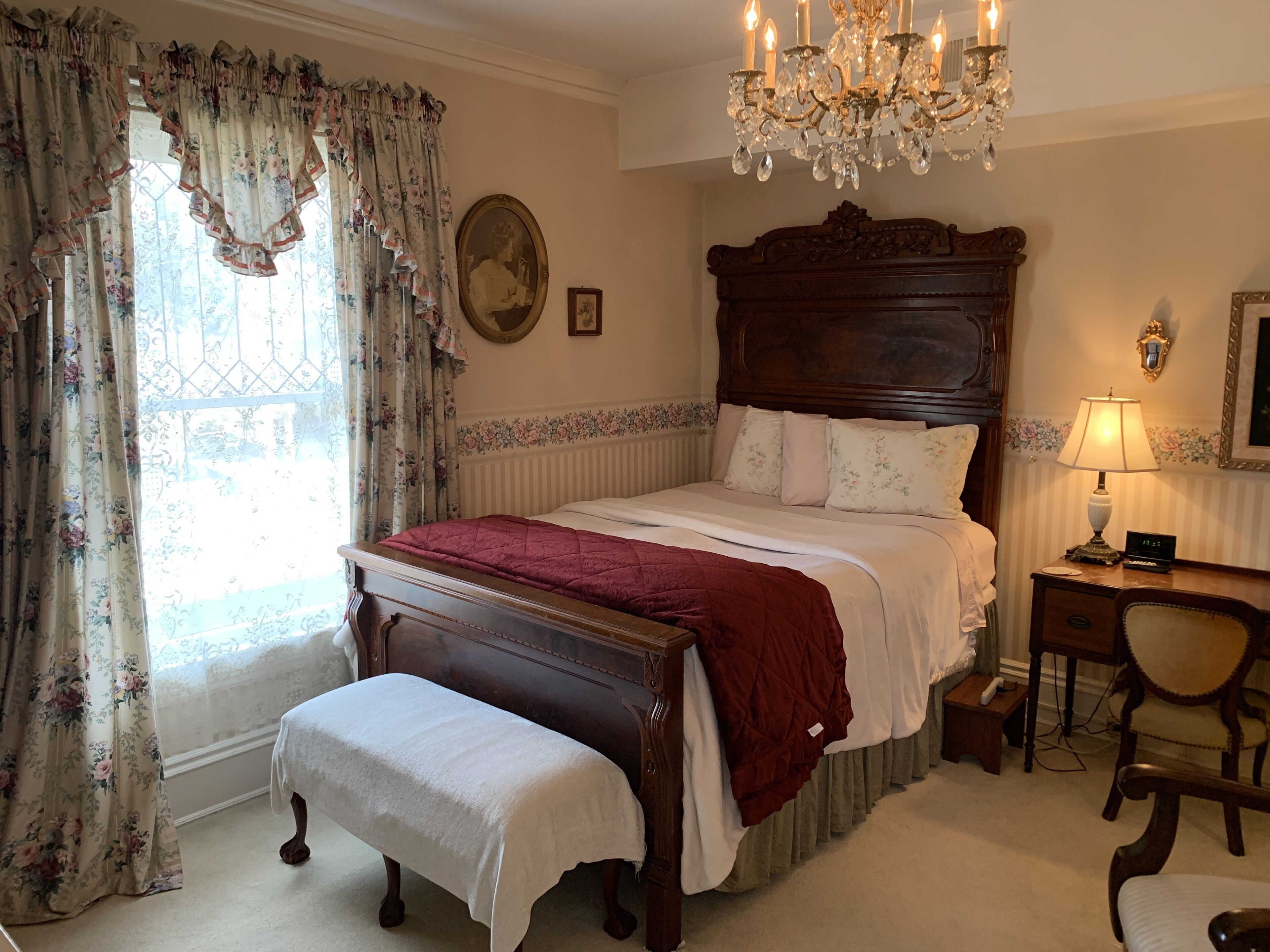 A bedroom with a wooden bed, a bench, a desk, and a chandelier.