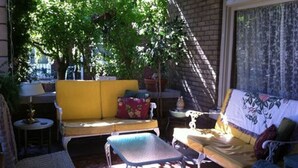 Un patio iluminado por el sol con un sofá amarillo, una silla azul y una pequeña mesa.