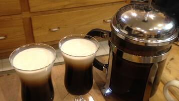 Two glasses of dark liquid on a wooden surface, a metal container with a lid, and a white object with a handle.