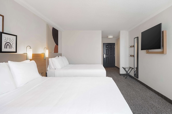A hotel room with two beds, a TV, a coat rack, and a door leading to another room. - Spark by Hilton Orangeburg (Orangeburg)