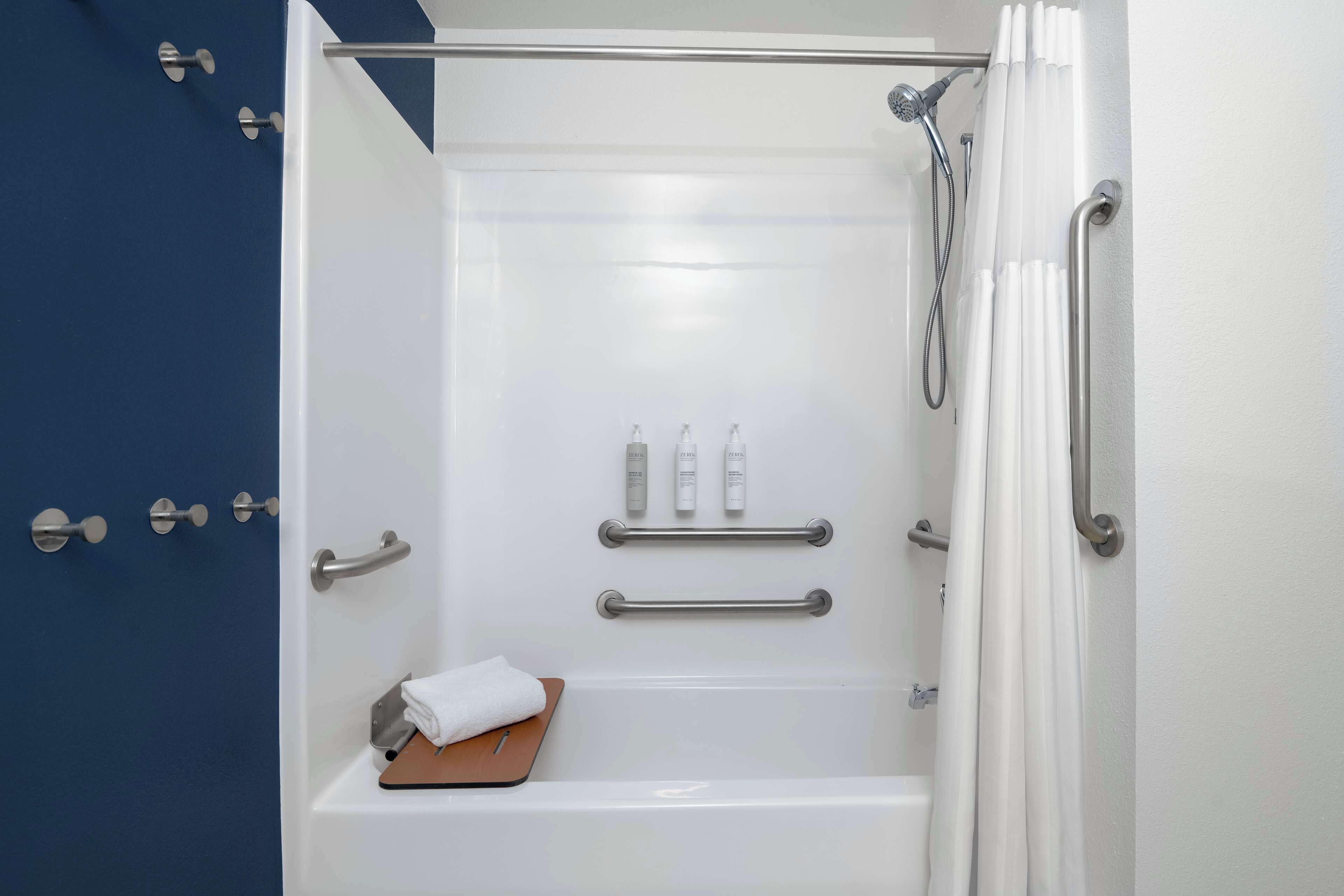 A modern bathroom with a bathtub, shower, and handrails.
