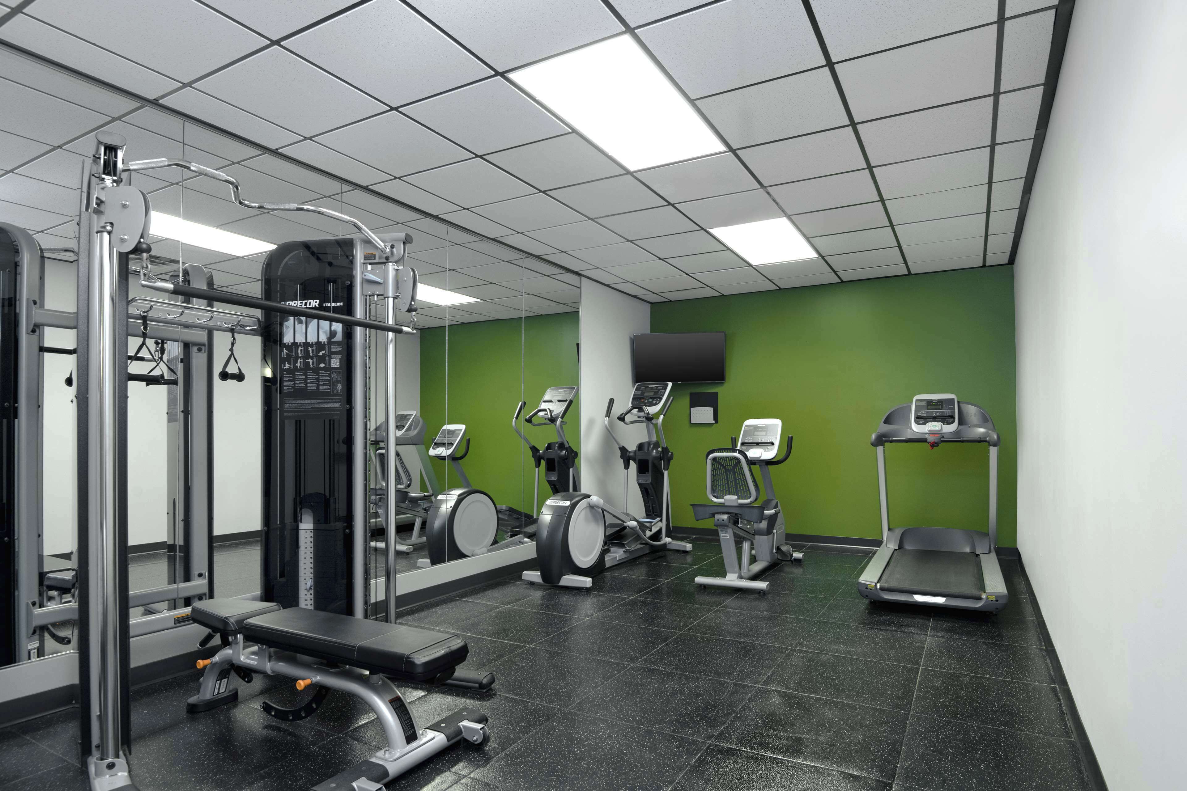 Een sportschool met diverse fitnessapparaten, waaronder een bankdrukpers, een squatsrek en loopbanden.