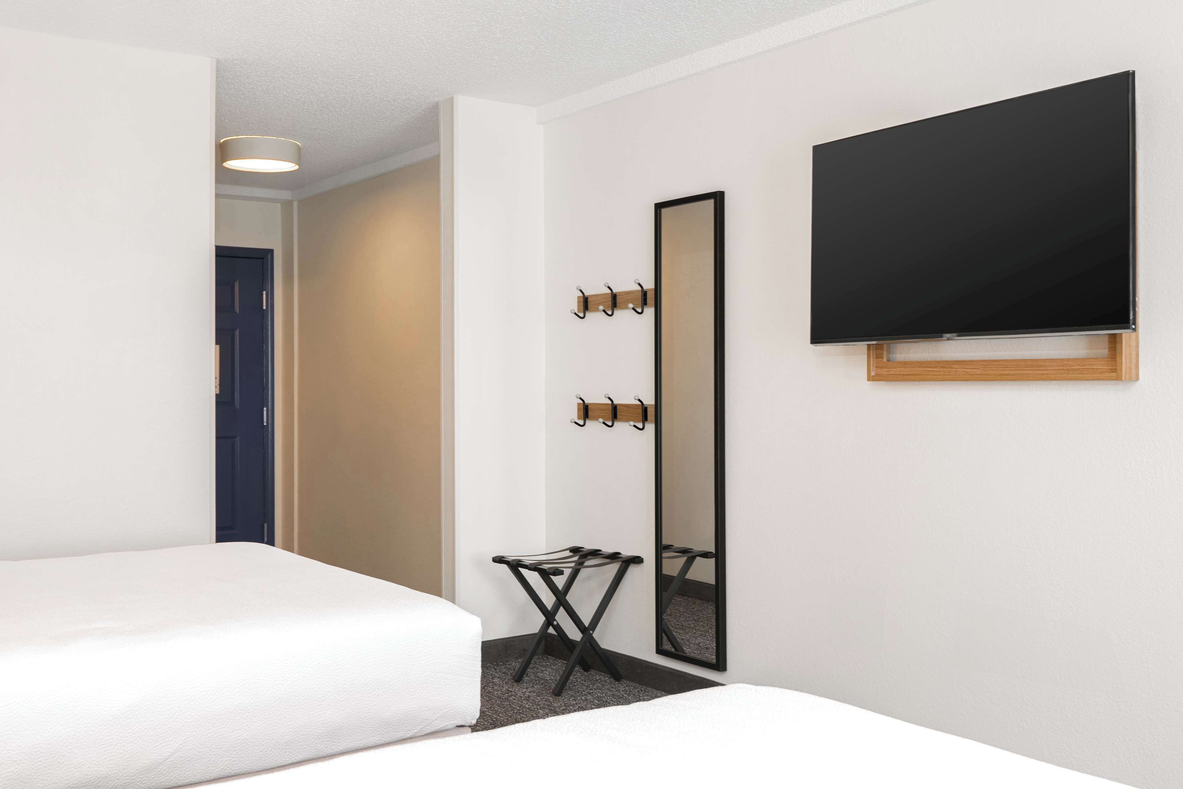 Une chambre d’hôtel avec un lit, un miroir, une télévision et un porte-manteau.