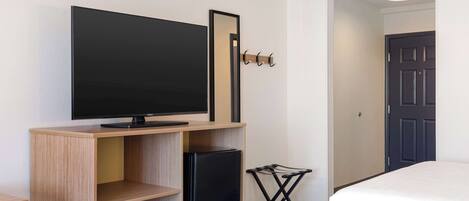 Une chambre d’hôtel équipée d’un téléviseur à écran plat posé sur un meuble en bois, d’un petit réfrigérateur, d’un porte-manteau, d’une chaise pliante et de deux lits.