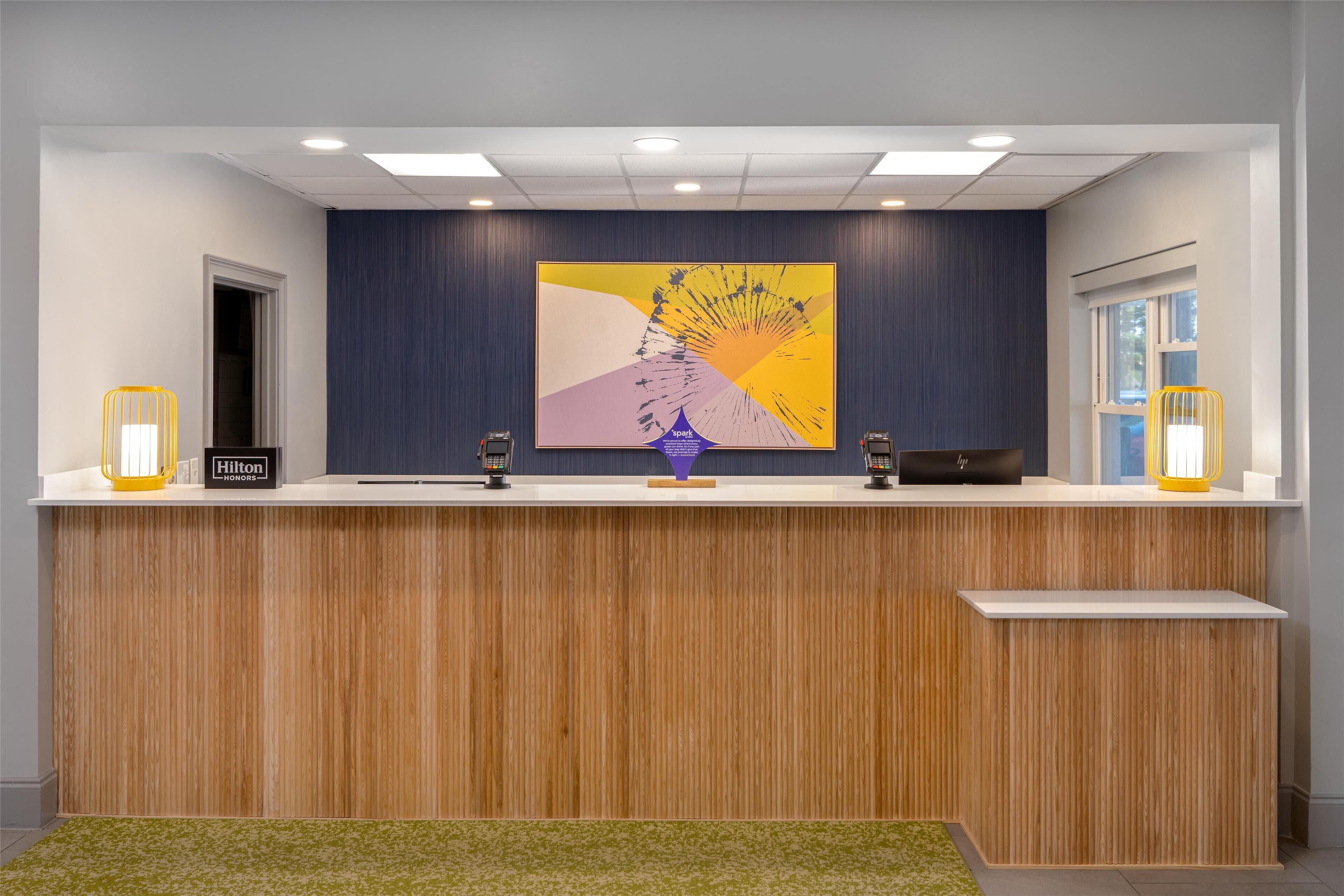 A hotel reception desk with a modern design, featuring a wooden finish and a large abstract artwork above it.