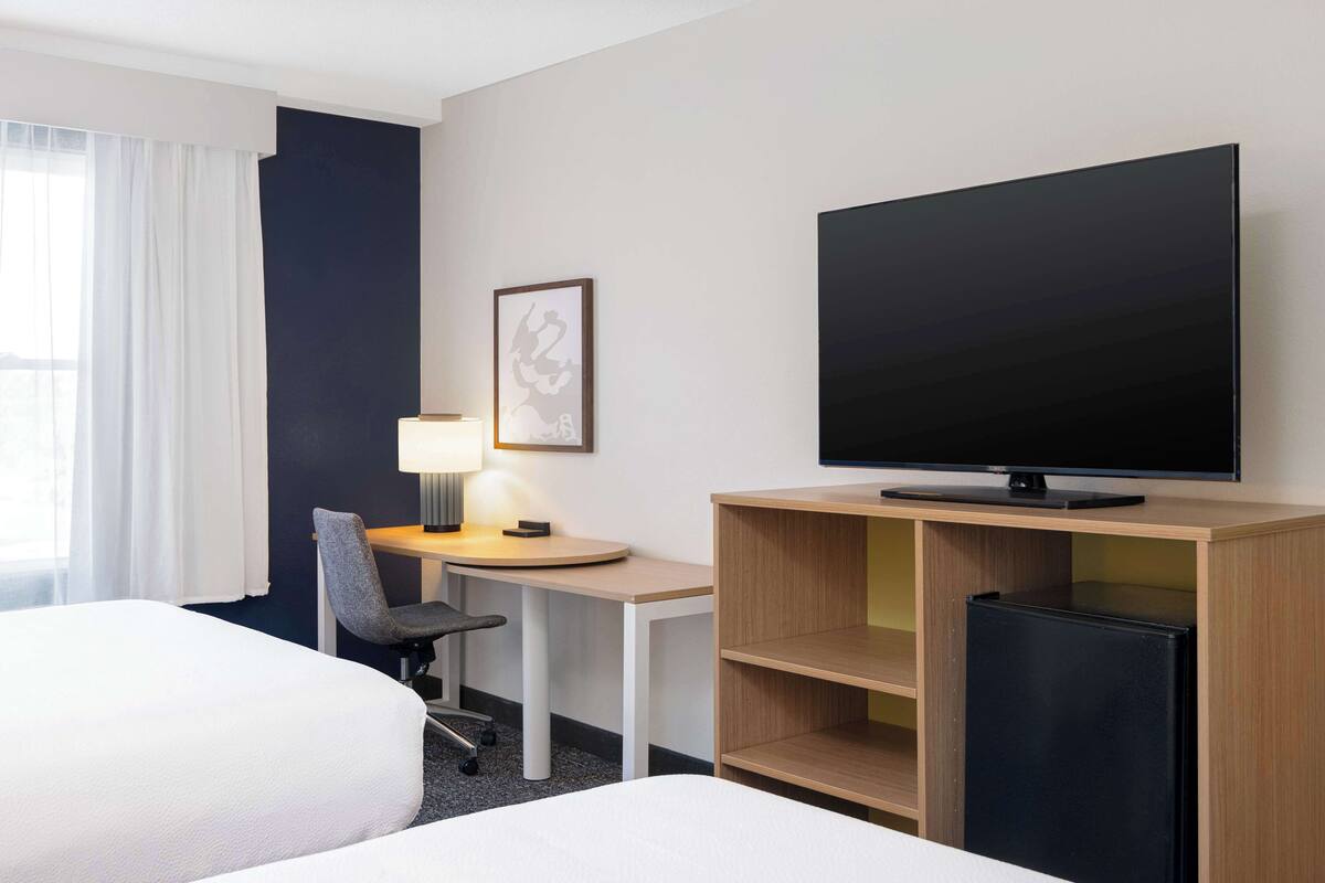 Habitación de hotel con dos camas, un escritorio con silla, televisión y un refrigerador pequeño.