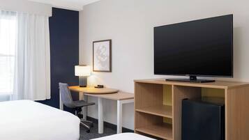 A hotel room with two beds, a desk with a chair, a television, and a small refrigerator.