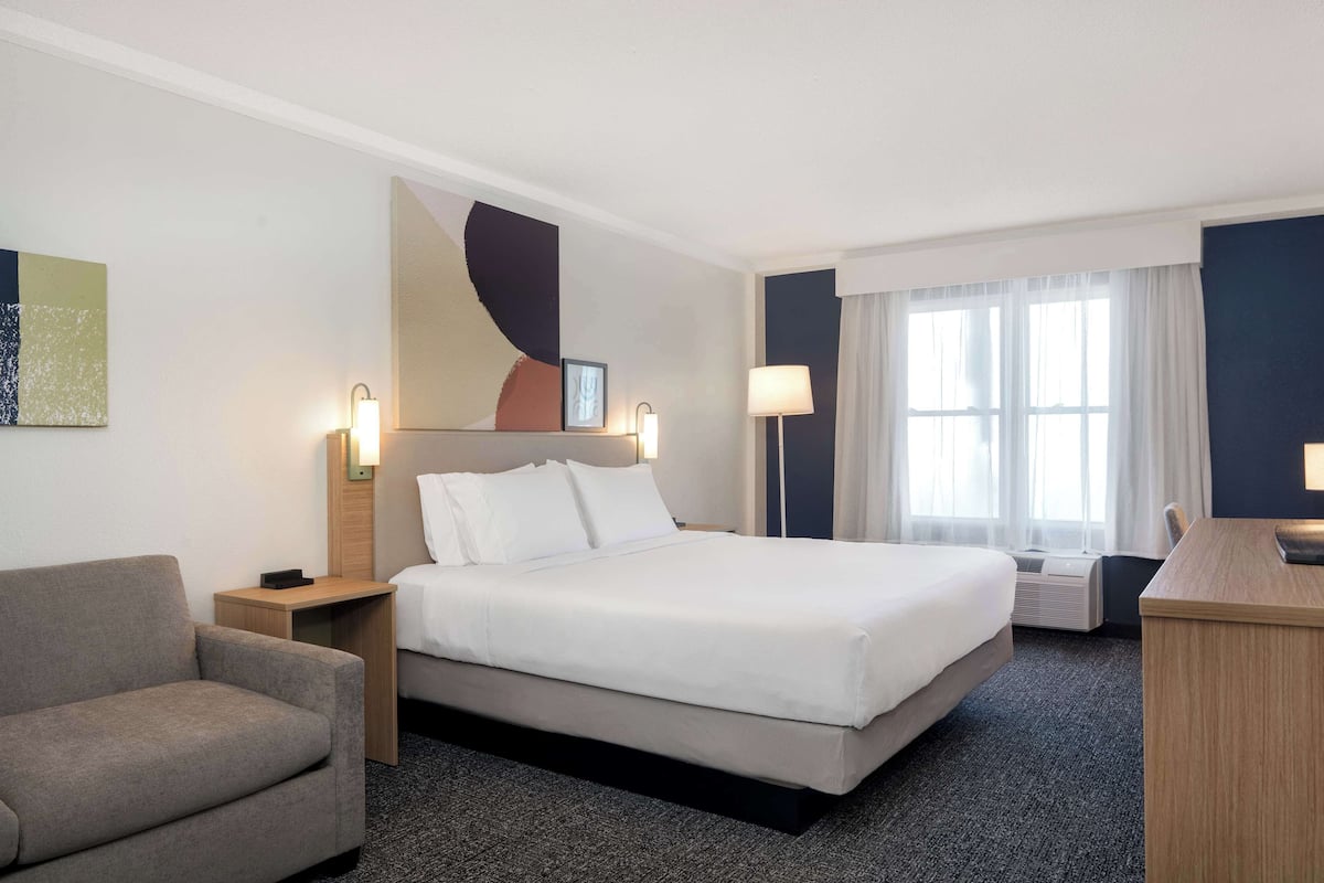 Una habitación de hotel con una cama grande, un escritorio, una silla y una mesita de noche con lámpara.