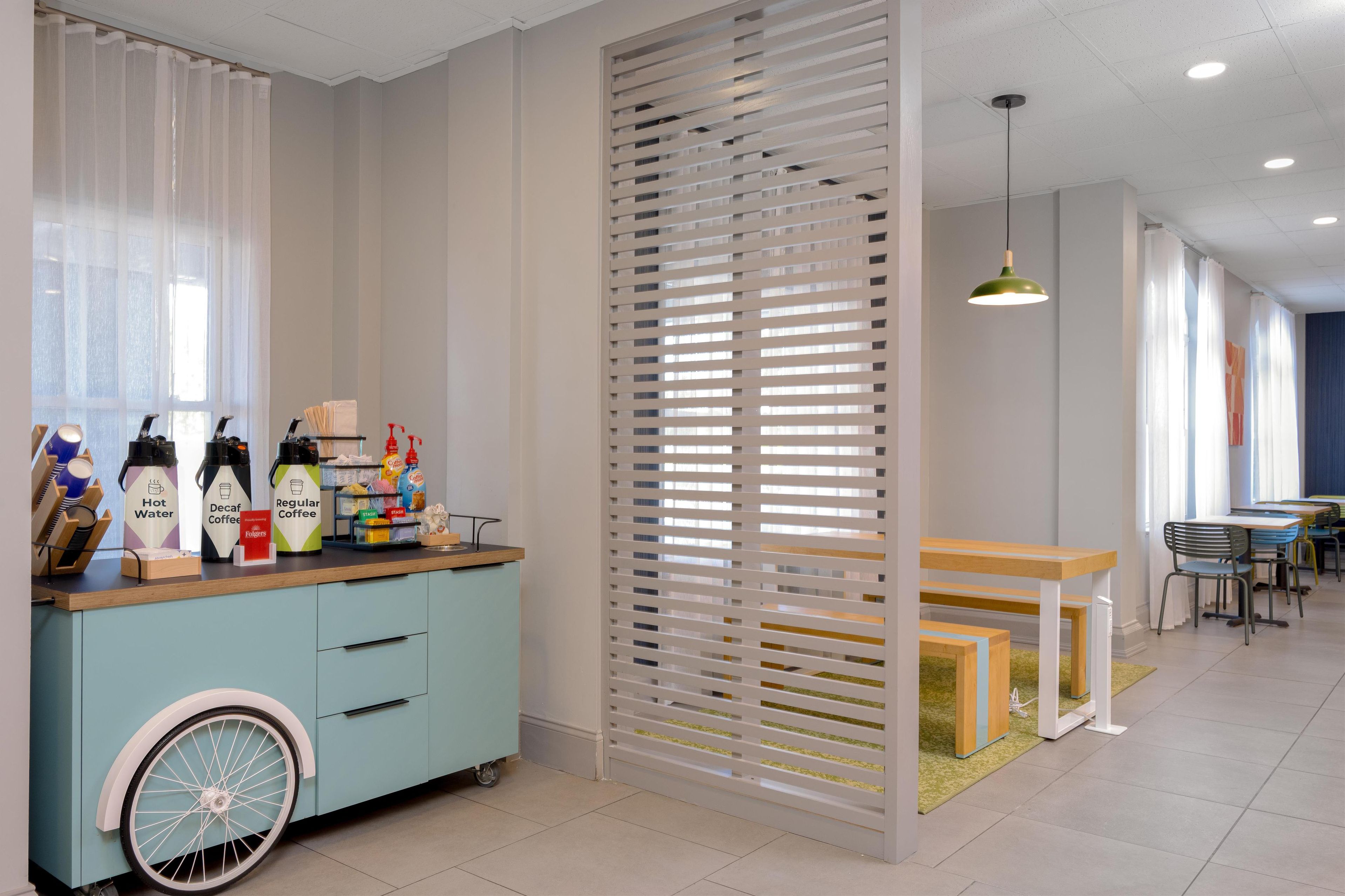 A modern cafe with a light blue counter, a bicycle wheel decoration, and a partition with horizontal slats.