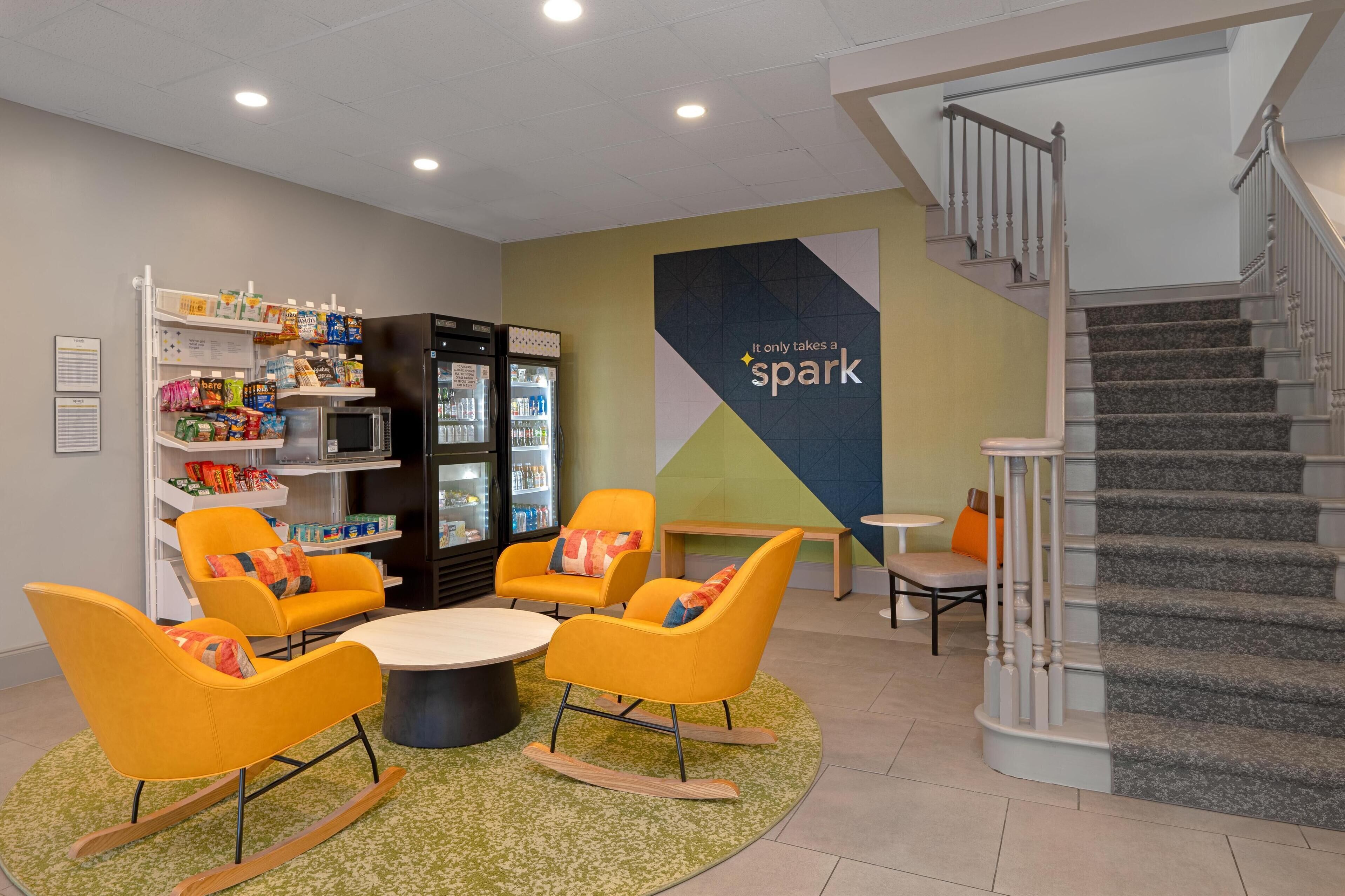 A modern lounge area with seating, a refrigerator stocked with beverages, and a staircase.