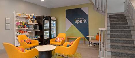 A modern lounge area with seating, a refrigerator stocked with beverages, and a staircase.