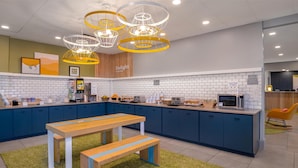 Una cocina moderna con una mesa y banco de madera, armarios azules y una lámpara colgante amarilla.