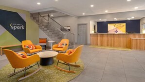 Un vestíbulo con mostrador de recepción, una escalera y una zona de estar con sillas anaranjadas.