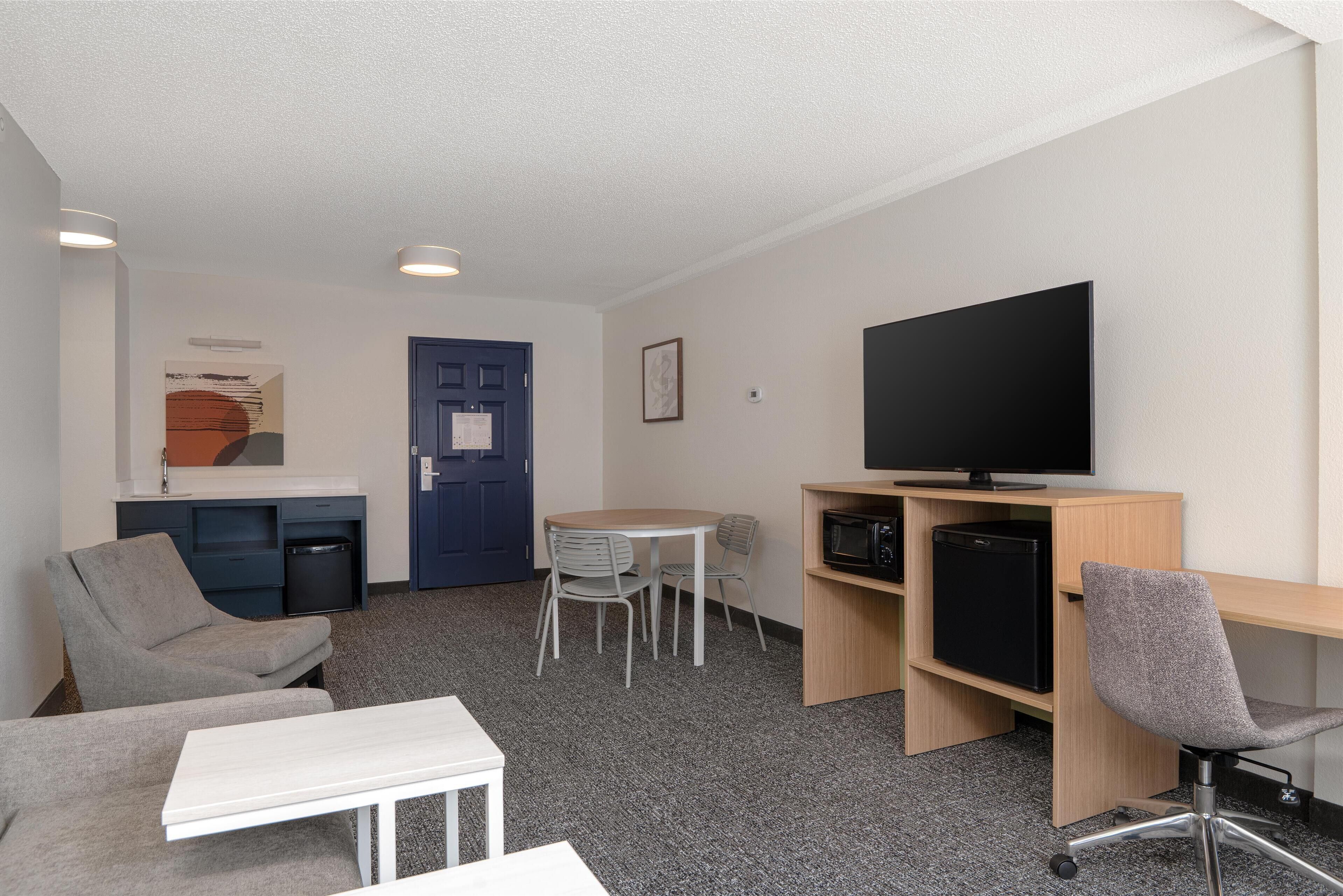 Ein kleines Hotelzimmer mit Sofa, Tisch, Fernseher, Schreibtisch mit Computer und Stuhl.