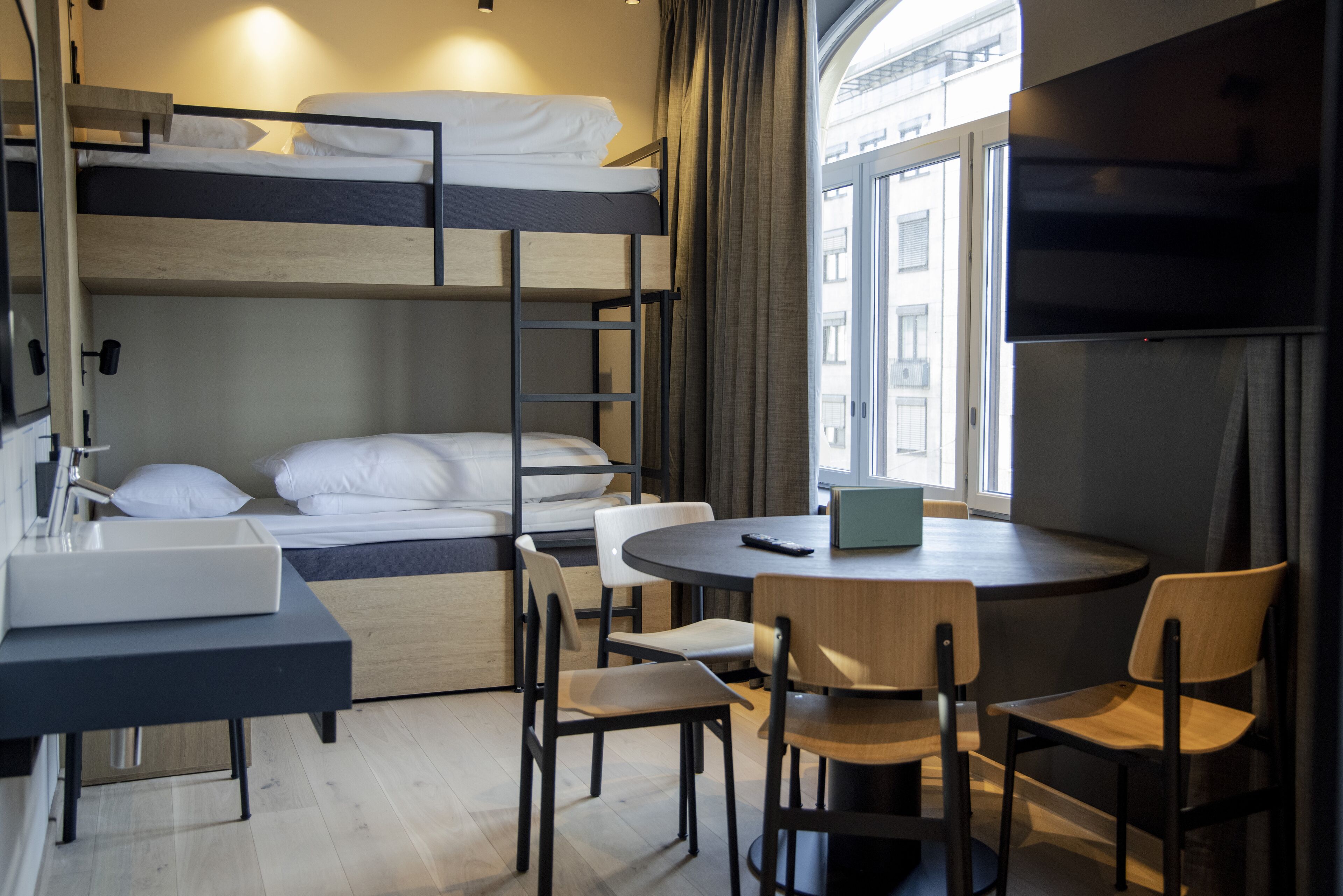 Une chambre avec un lit superposé, un lavabo, des chaises et un téléviseur.
