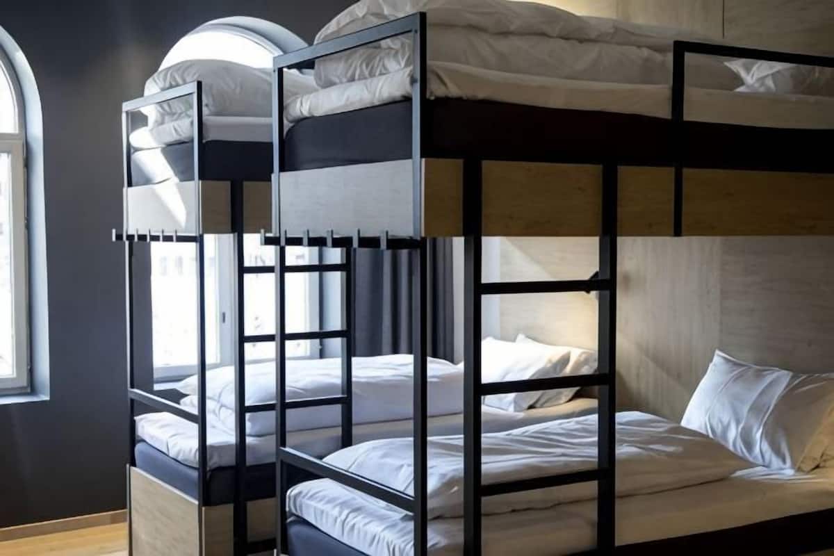 Un lit superposé avec une structure en bois, une literie blanche et une fenêtre laissant entrer la lumière naturelle.