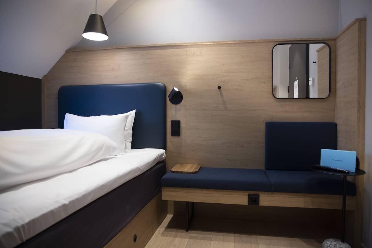 Une chambre à coucher moderne avec un lit, un banc, un ordinateur portable et un miroir.