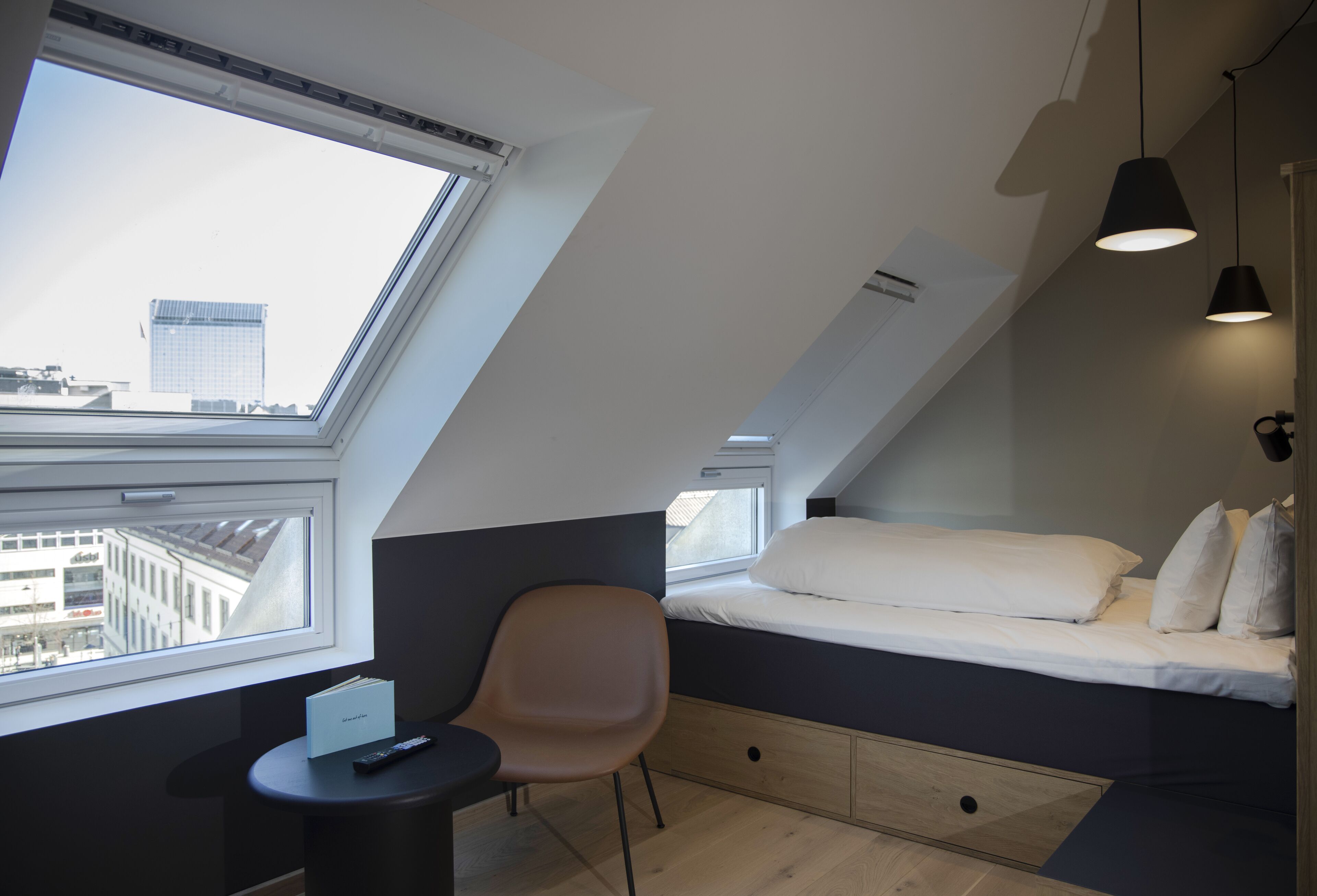 Un dormitorio moderno y compacto con tragaluz, una cama, una silla y una mesita.