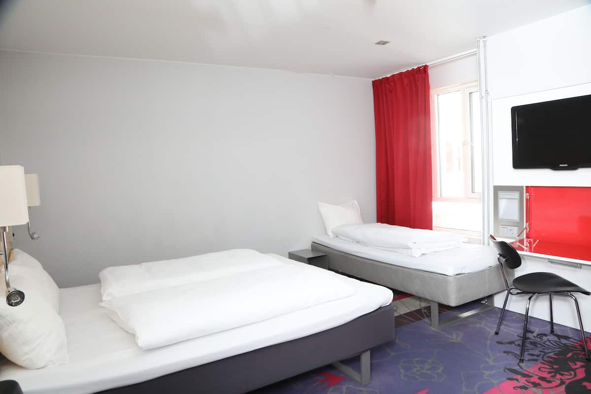 Une chambre d’hôtel avec deux lits, un téléviseur fixé au mur et une fenêtre avec des rideaux rouges.
