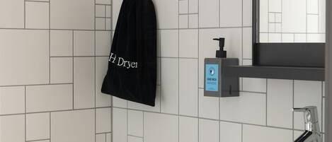 Un baño con lavamanos blanco, un espejo, dispensador de jabón para manos y una bolsa negra colgada en la pared.