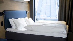 Una cama bien hecha con sábanas blancas, un cabecero oscuro y una mesita de noche con una lámpara.