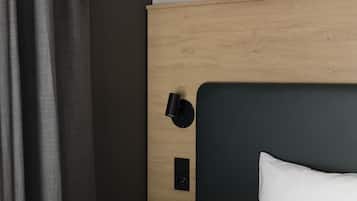 Cama bem arrumada com lençóis brancos, cabeceira escura e luminária preta fixada na parede.