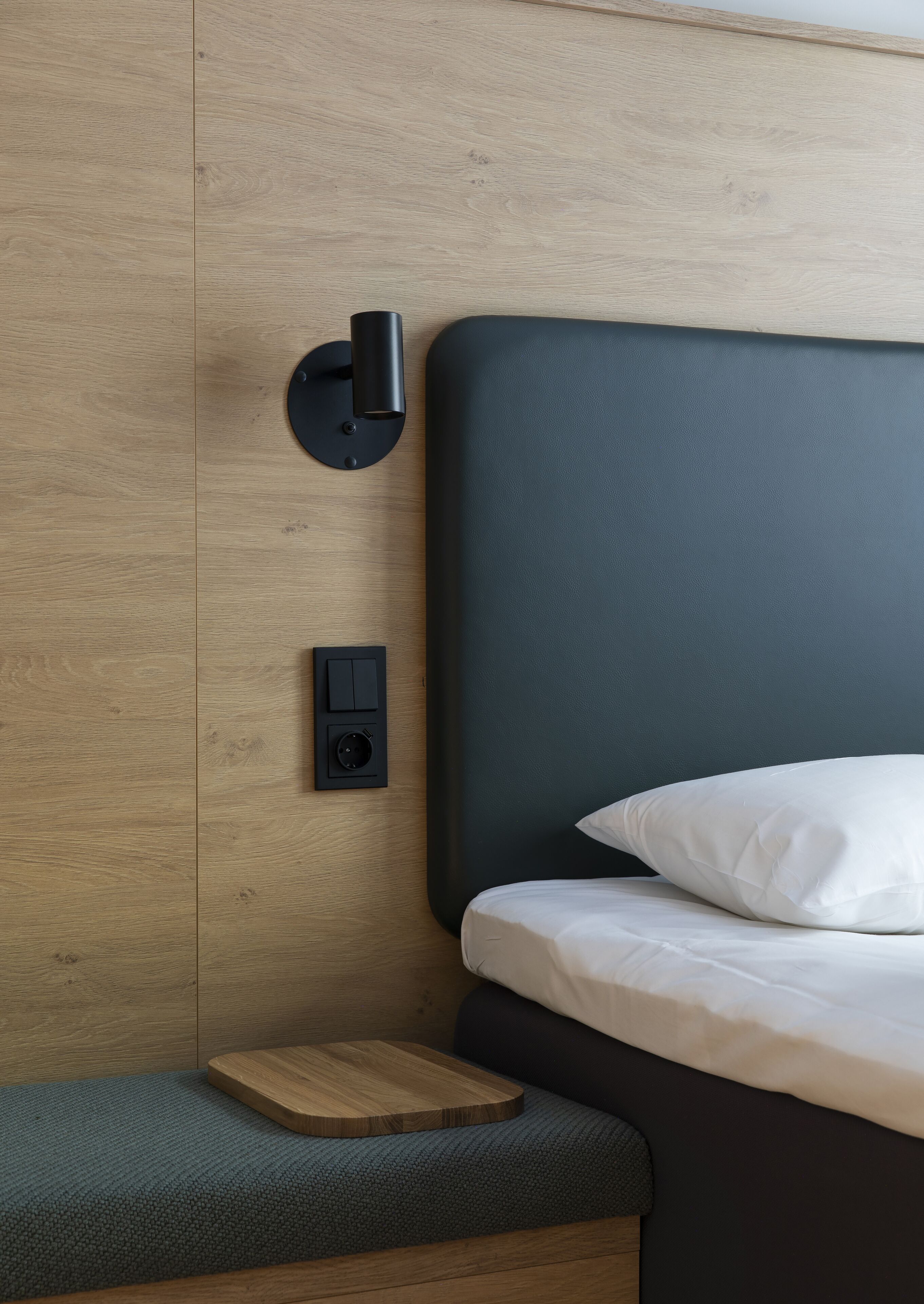 A modern bedroom with a wooden headboard, a bedside table, and a wall-mounted light fixture.