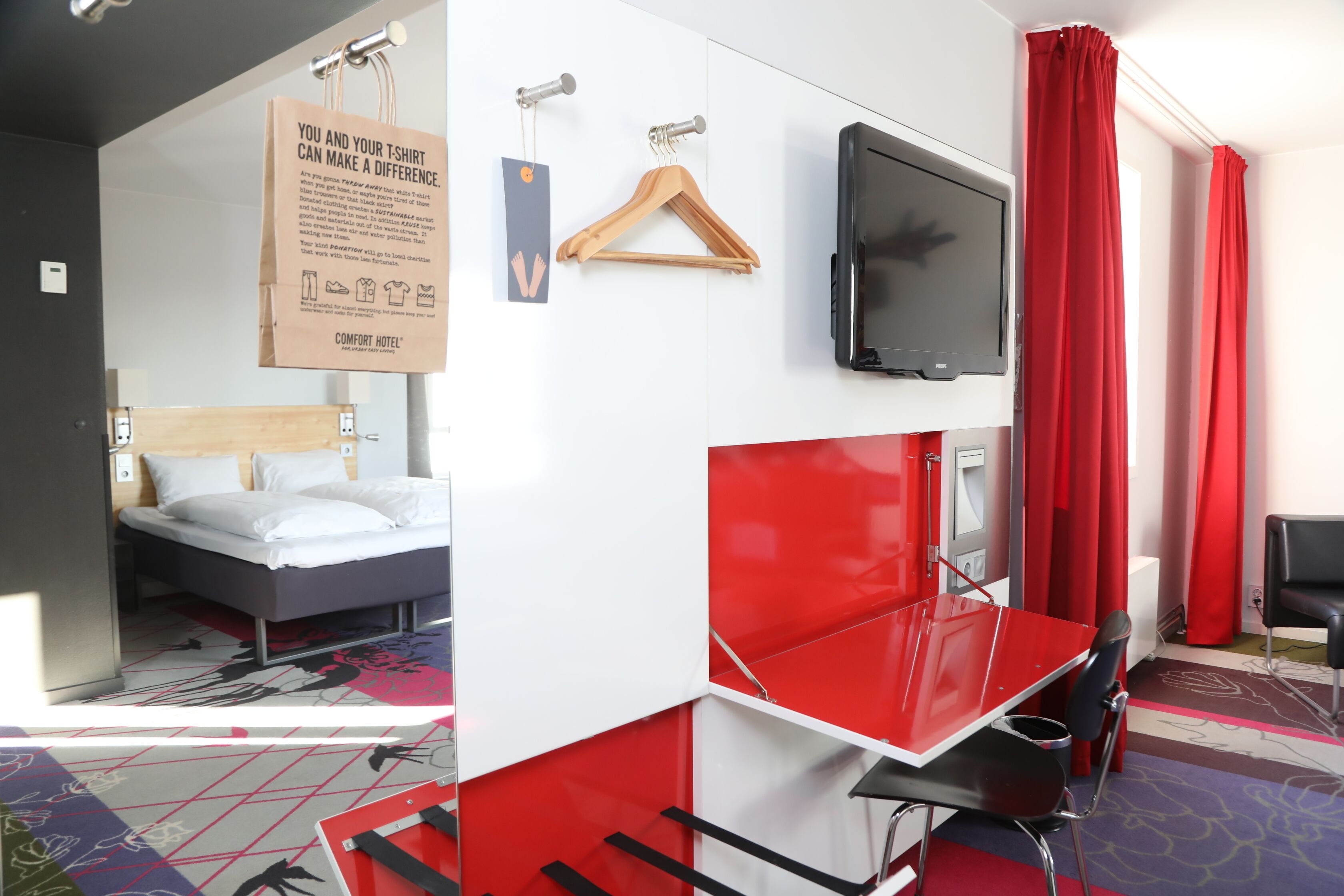 A hotel room with a bed, a TV, a red desk, and red curtains.