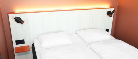 A double bed with white linens, a wooden nightstand, and a wall-mounted light fixture.