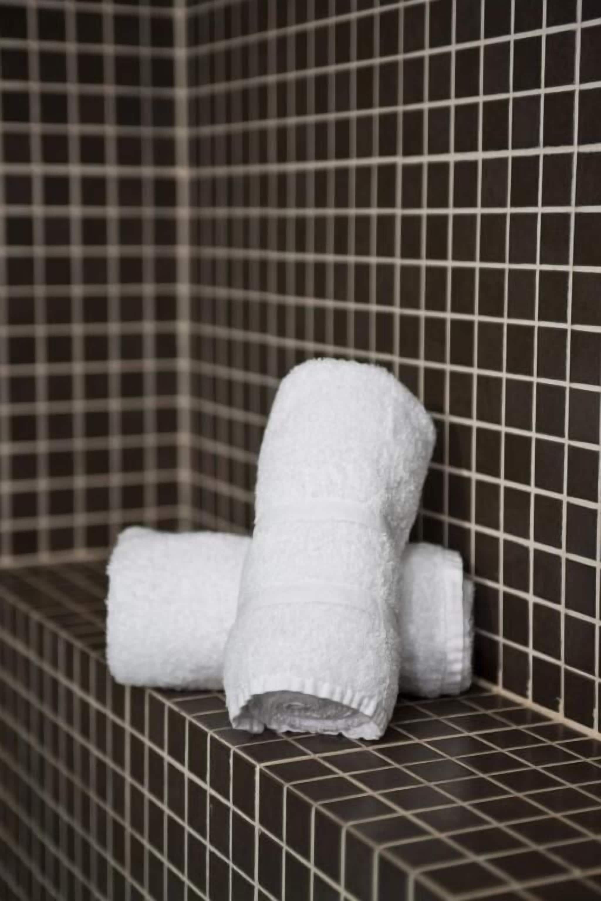 A tiled wall with a towel rack holding rolled towels.