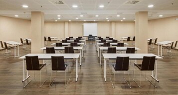 Uma sala de conferências com várias mesas, cadeiras, um quadro branco e uma tela de projeção.