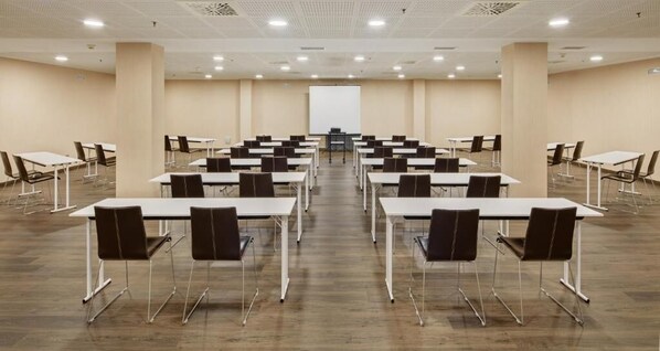 Une salle de conférence équipée de plusieurs tables et chaises, d’un tableau blanc et d’un écran de projection.