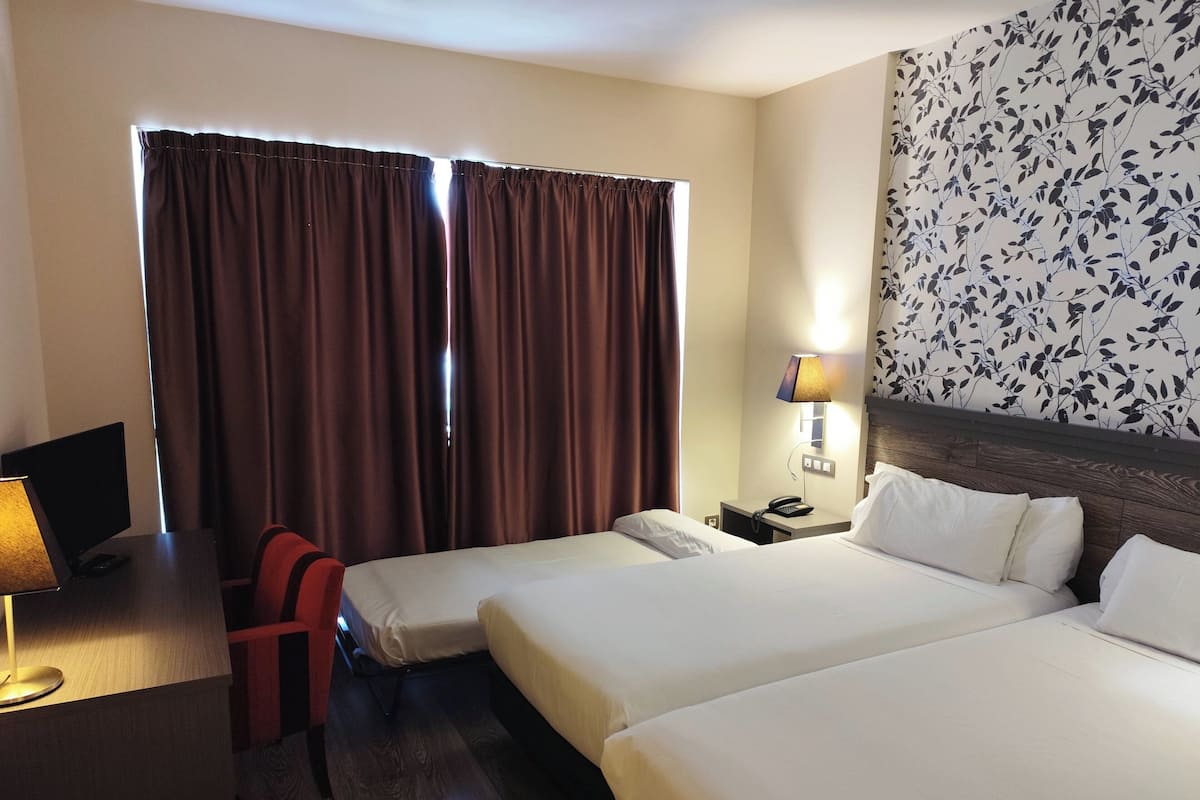 Habitación de hotel con dos camas, un escritorio con lámpara, una silla, un teléfono en la mesita de noche y una ventana con cortinas.
