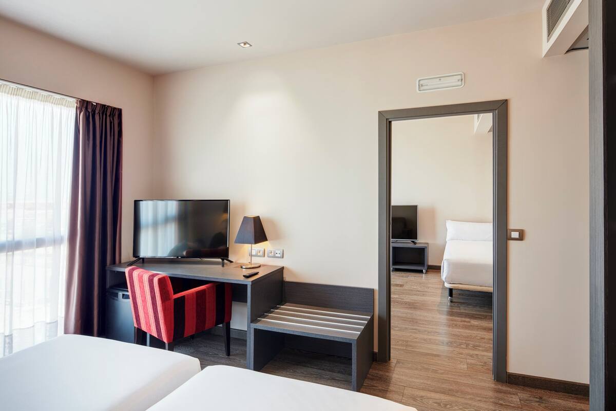 Een hotelkamer met een bed, een bureau met stoel, een televisie, een lamp en een spiegel.