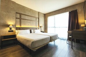 Habitación de hotel con dos camas, un escritorio y un ventanal grande con cortinas.