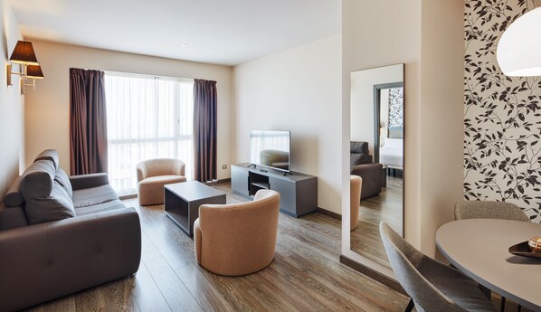 Un salon moderne avec un canapé, des fauteuils, une table basse et un téléviseur posé sur un meuble.